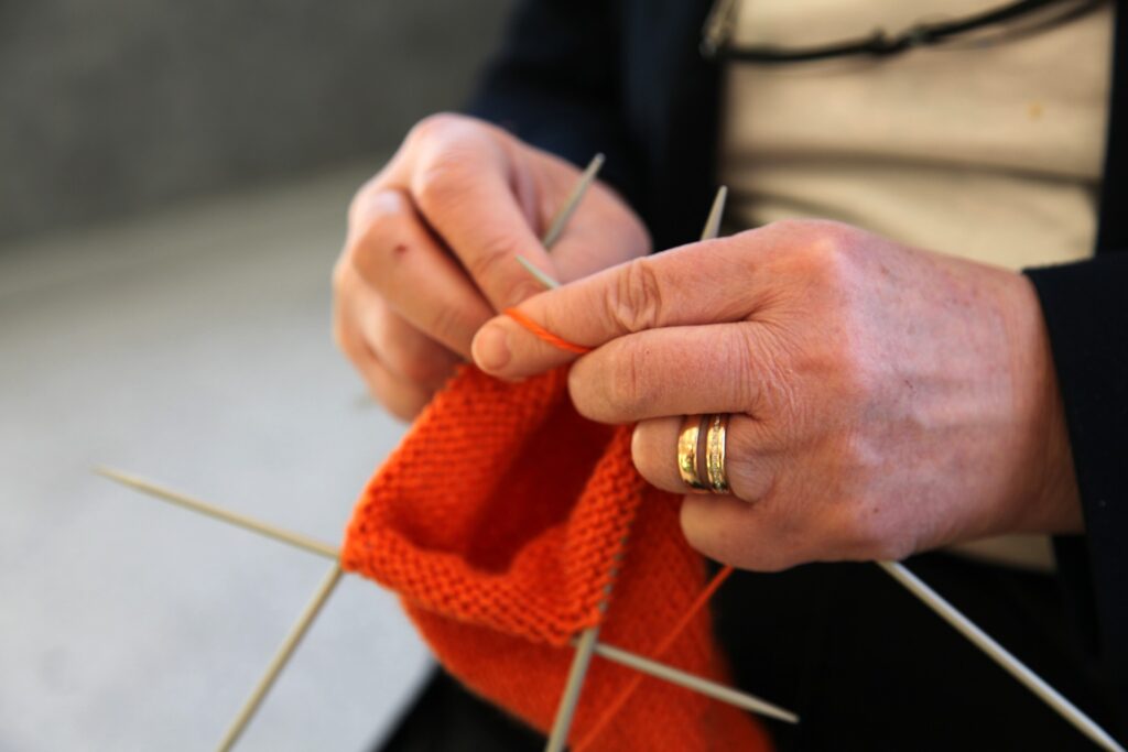 A woman knitting a piece of orange yarn with knitting needles.