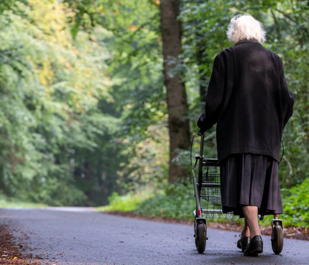 An elderly woman walking down a road with a walker.